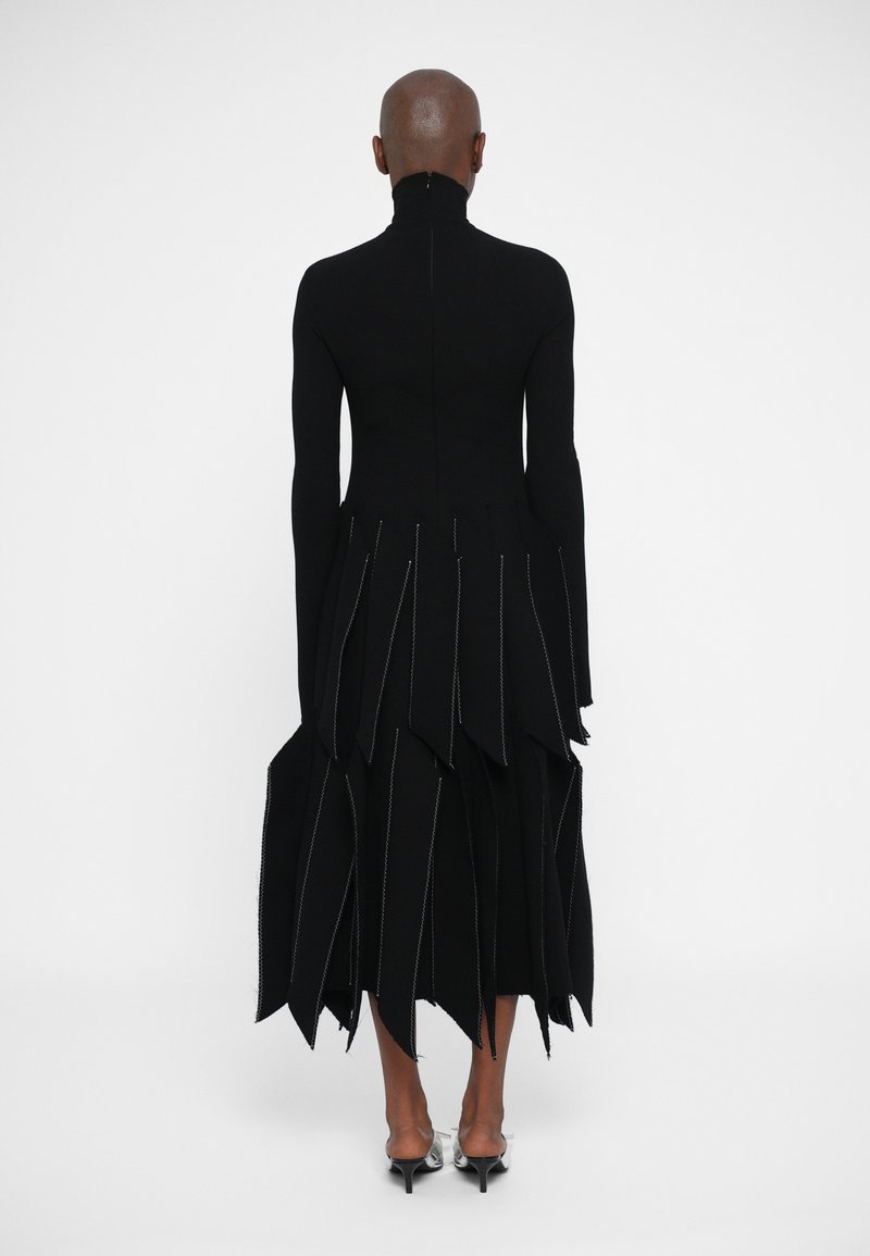 Black dress with a high neck, long sleeves, and a layered skirt featuring irregular, pointed edges and contrasting stitching details.