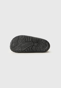 Black rubber outsole with textured tread patterns and logo. Features a rounded heel and a flexible design for traction and comfort.