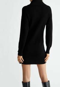 Schwarzes geripptes Strickkleid mit hohem Kragen, langen Ärmeln und figurbetonter Silhouette, mit einem Saum, der knapp über dem Knie endet.