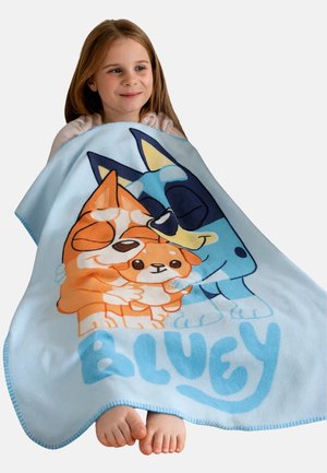 Blue blanket featuring Bluey and Bingo cartoon characters in vibrant colors, soft texture, and blue trim. Child holds it on their lap.