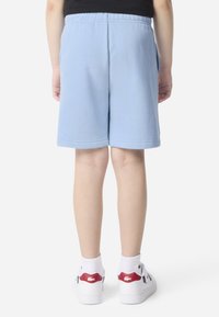 Shorts en coton bleu clair avec une taille élastique, coupe droite, sans motifs visibles, assortis à des chaussures blanches avec des accents rouges.