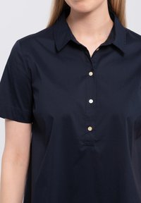 Donkerblauw shirt met korte mouwen en een puntige kraag, voorzien van een knoopsluiting met drie lichte knopen en een gladde, gestructureerde stof.