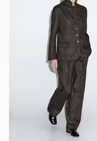 Costume ajusté gris charbon en tissu texturé ; comprend un col montant, un devant à simple boutonnage avec des boutons, et un pantalon à jambes larges.