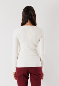 Maglietta a maniche lunghe a coste in off-white con una silhouette aderente e scollo rotondo, abbinata a pantaloni borgogna. Texture liscia in tutto.