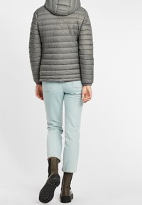 Giacca piumino grigia con cuciture orizzontali e cappuccio, abbinata a jeans azzurri chiari e stivaletti neri, vista da dietro.