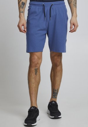 Blauwe textuurshorts met een elastische tailleband en trekkoord. Gevered met zwarte sportieve schoenen. De shorts hebben zijzakken.