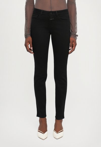Jean skinny noir en denim lisse, avec des poches avant, une fermeture à bouton et une coupe ajustée jusqu'aux chevilles.