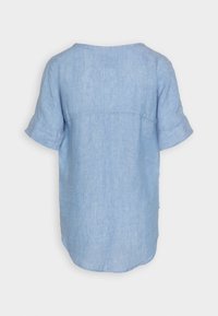Chemise en lin bleu clair avec des manches courtes retroussées, un col rond et un ourlet légèrement arrondi. Présente une couture dans le dos.