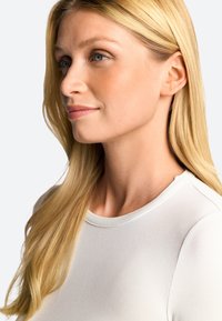 Lähedane pilt inimesest, kellel on sirged, pikad blondid juuksed, seljas kitsas valge särk ümarate kaelustega ja sileda tekstuuriga.