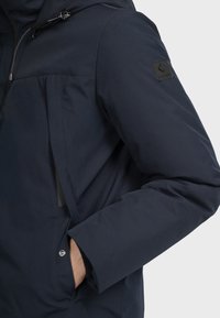 Námořnická modrá zateplená bunda s kapucí, s texturovanou tkaninou, zipem vpředu a logem na rameni.