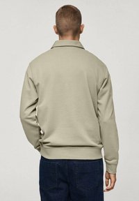 Jasno khaki sweatshirt z kołnierzem, luźny krój, ściągacze przy rękawach i u dołu, pokazany z tyłu. Gładka tekstura, minimalne detale.