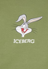 T-shirt verde in cotone con un cartone animato di un coniglio dalle orecchie lunghe, un ampio sorriso e il testo "ICEBERG" in bianco sotto il design.