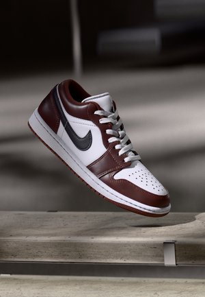 Niedrigschuh-Sneaker aus weißem Leder mit maroonfarbenen und schwarzen Akzenten. Verfügt über eine perforierte Zehenkappe, graue Schnürsenkel und eine strukturierte Gummisohle.