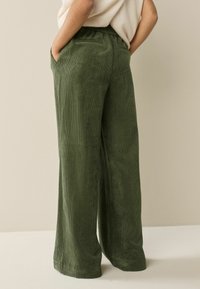 Green corduroy pants with a wide leg design, featuring an elastic waistband and pocket detail, shown from a side and back view.