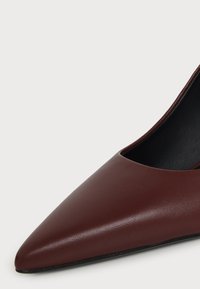 Gros plan d'une chaussure plate marron à bout pointu en cuir lisse avec une ouverture basse et une doublure intérieure noire.