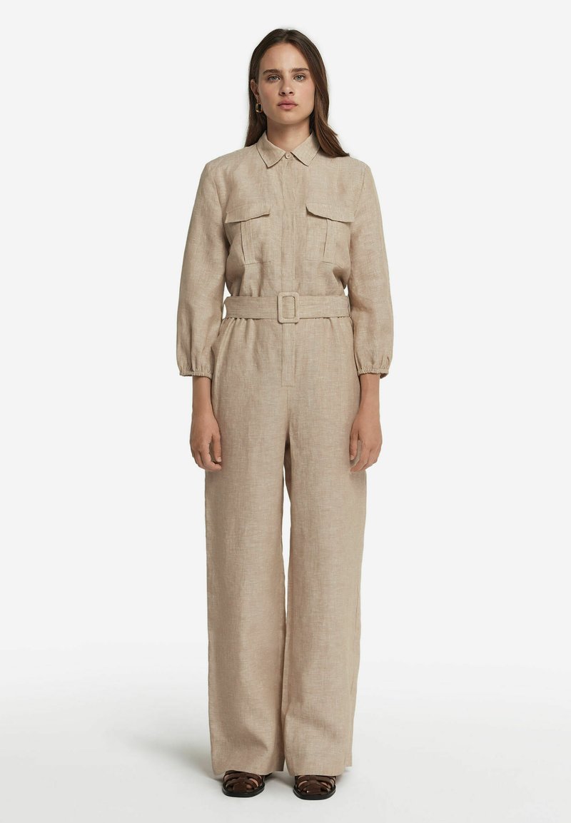Beige Leinen-Overall mit einem Kragen-Ausschnitt, langen Ärmeln, zwei Brusttaschen, tailliertem Gürtel und weitem Bein-Design. Glatte Textur.