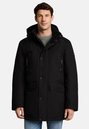Man wearing a black hooded winter coat with buttons and zippered pockets, standing against a white background.