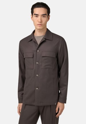 Chaqueta marrón de botón con dos bolsillos en el pecho y un cuello recto. Textura suave; diseñada con un corte relajado y detalles de costura sutiles.