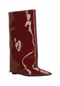 Botte en cuir verni rouge avec un design élégant à hauteur de cheville, bout pointu et finition brillante. L'ourlet supérieur courbé crée une silhouette unique.