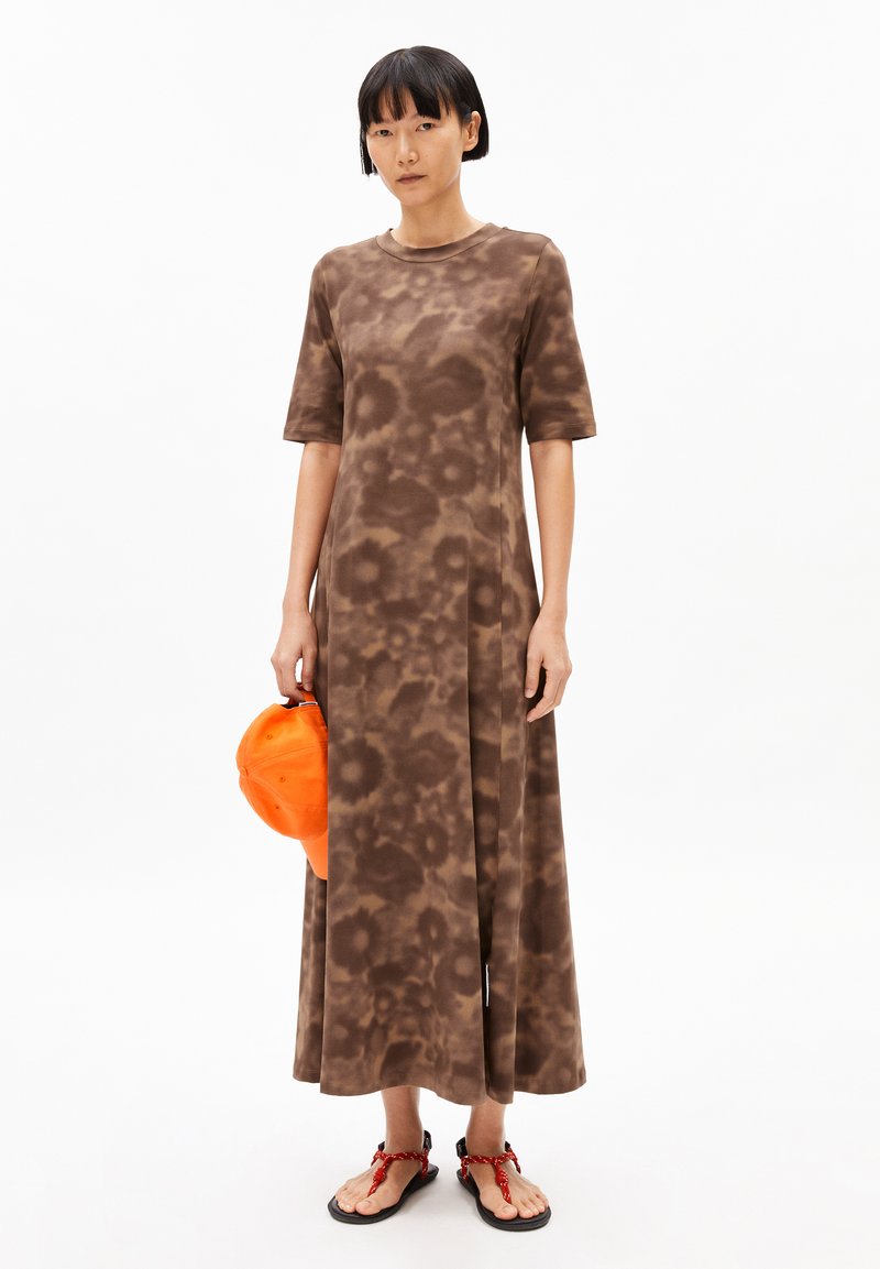 Brown tie-dye t-shirt dress with short sleeves, flowing design, side slit, worn with an orange cap and red sandals.