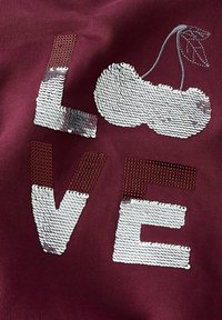 Tessuto color mogano con lettere in rilievo di paillettes bianche che formano la parola "LOVE", accompagnato da un design di ciliegia in paillettes con foglie verdi.