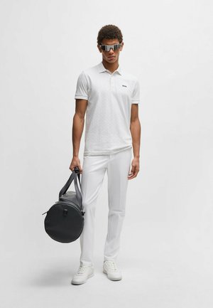Weißes strukturiertes Polohemd mit einem Logo, getragen mit weißen Hosen und Sneakers. Schwarze runde Sporttasche in der Hand und Sonnenbrille mit spiegelnden Gläsern getragen.