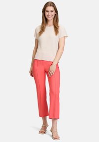 Light beige textured top with short sleeves paired with bright coral cropped trousers. The outfit features a relaxed fit and flat shoes.