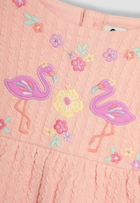 Roosa kudumine, millel on kaks broderitud flamiingo, lilleaktsendid ja tekstureeritud nööride muster. Selja kaela sulgemine, volangiga ääre detail.