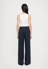 White ribbed tank top paired with navy wide-leg trousers, featuring a smooth fabric and a fitted waistband. Back view, minimal detail.