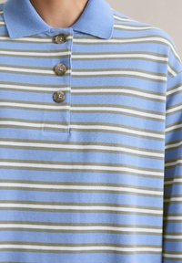 Polo shirt rayé avec une base bleu clair et des rayures horizontales en vert foncé et blanc. Présente un col et une patte de boutonnage.