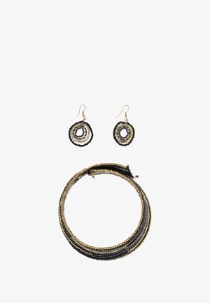 Fekete és arany gyöngy ékszerszett, amely egy tekeredett nyakláncból és ovális, lógó fülbevalókból áll, rétegezett körformákkal. Texturált felületek, fényes kiegészítők.