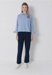 Ljusblå skjorta med långa ärmar, marinblå byxor och vita sneakers. Skjortan har en bröstficka och en avslappnad passform.