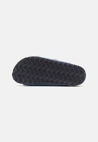 Semelle de chaussure avec une texture ondulée, principalement noire avec des accents bleus. Présente un profil plat et un design de semelle minimal pour une traction optimale.