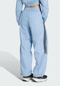 Ljusblå, lätta adidas träningsbyxor med svarta sidosträck, elastisk midja och smala fållar. Lämpliga för aktivt bruk.