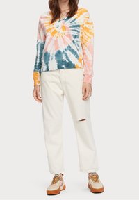 Felpa tie-dye multicolore in toni pastello, abbinata a pantaloni bianchi con strappo al ginocchio e sneaker beige con suola marrone.