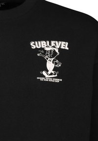 Zwarte sweatshirt met een witte grafische illustratie van een personage in een overall, met "SUBLEVEL" en tekst eronder in vette letters.