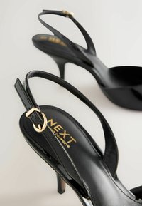 Melni papēžu sandales ar spīdīgu virsmu, slaidu dizainu, smailu purngalu un zelta krāsas sprādzes detaļu. Zīmola nosaukums drīkst no iekšpuses.