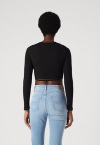 Sort cropped langærmet top med rund halsudskæring og guldtråd, parret med lyseblå højtaljede jeans med baglommer.