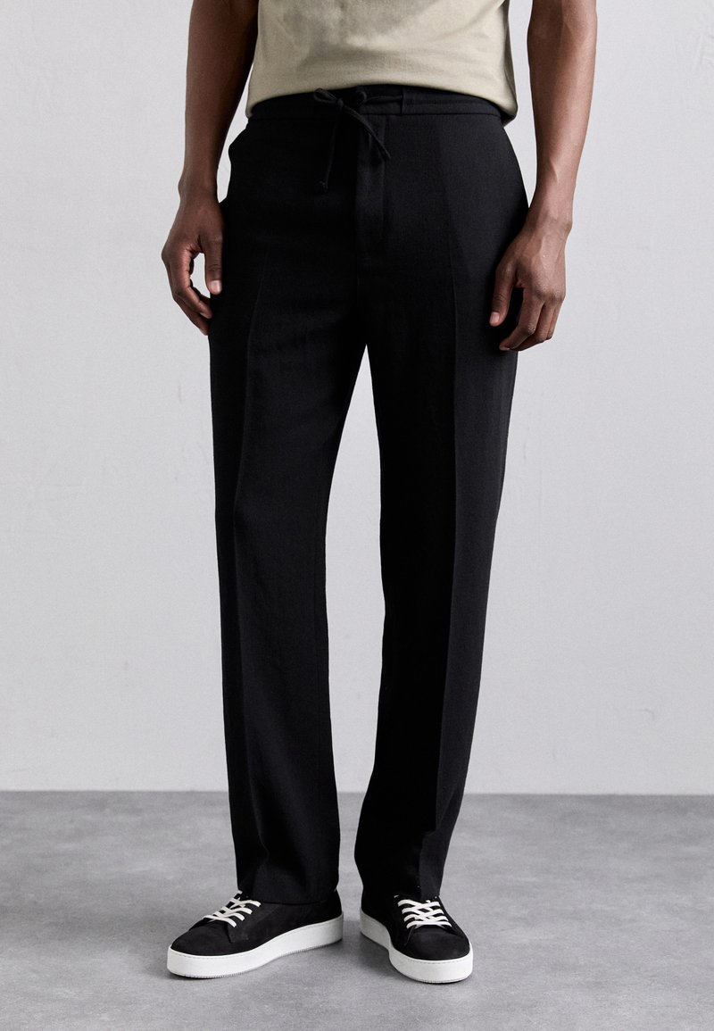 Czarne, dopasowane spodnie z elastycznym paskiem. Gładki materiał o prostym kroju. Połączone z czarnymi trampkami z białymi podeszwami i sznurowadłami.