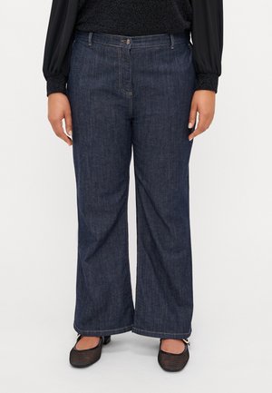 Jean en denim foncé à jambes larges avec fermeture éclair et bouton, dotés de deux poches avant et d'une coupe décontractée. Complétés par des chaussures plates en maille texturée.