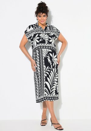 Schwarzes und weißes kurzärmeliges Kleid mit floralem Muster, knielang, mit Kragen und einem entspannten Schnitt. Glatte Stofftextur, kombiniert mit schwarzen Riemchenheels.