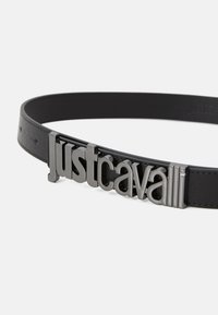 Svart lærbelte med en blank svart metallspenne som har preget teksten "justcavalli." Glatt overflate og elegant design.