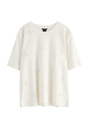 Hvid kortærmet T-shirt med rund hals, prydet med teksturerede sløjfer jævnt fordelt over stoffet. Glat, blødt materiale.