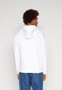 Hvit hettegenser med avslappet passform, laget av strukturert stoff og ribbede mansjetter. Brukt med blå avslappede jeans.