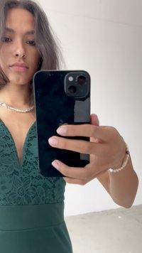 Žalia nėriniuota suknelė su V formos iškirpte, tekstūruota liemenė ir lygi sijonas. Apsivilkusi perlo karolius ir apyrankę, laiko išmanųjį telefoną.