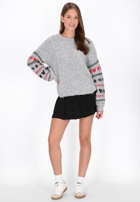 Lichtingrij grijze fuzzy trui met patroonmouwen die rode en zwarte hartontwerpen bevatten, gecombineerd met een zwarte geplooide rok en witte sneakers.