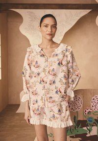 Dwuczęściowy komplet piżamowy w jasnoróżowy wzór kwiatowy. Bluzka z falbankami na rękawach i koronkowym kołnierzykiem; szorty ozdobione koronkową lamówką. Miękka faktura materiału.