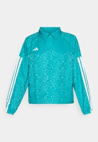 Tealfärgad Adidas-jacka med blommönster, vit tre-linjig design på ärmarna, tryckknappsframsidan och krage på en enkel bakgrund.