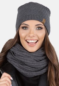 Grå strikket beanie med ribbede detaljer og et lædermærke. Matcher med et gråt tørklæde, der har et tekstureret, lagdelt udseende.