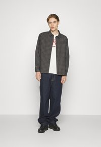 Langeærmet sort og grå ternet skjorte over en hvid grafisk t-shirt, parret med løse mørke jeans og sorte sneakers.